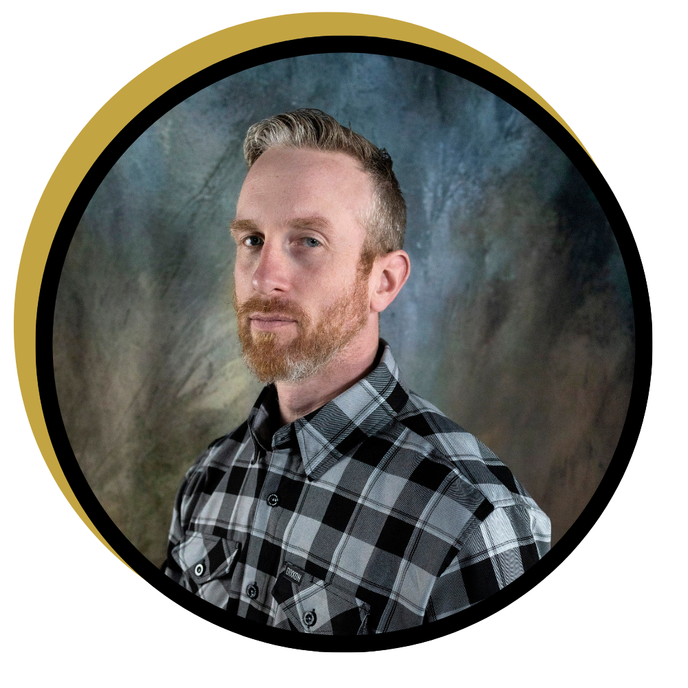 Steve McGill, motocross trainer, wearing a black and white plaid shirt, posed against a dark studio backdrop